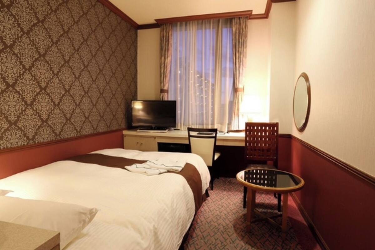 Ein Hotelzimmer mit Bett, Schreibtisch mit Fernseher, Stuhl und kleinem Tisch.