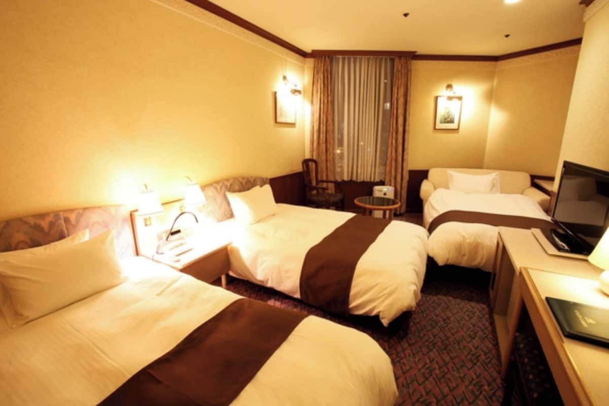 Ein Hotelzimmer mit zwei Betten, einem Schreibtisch, einem Stuhl und einem Fernseher.
