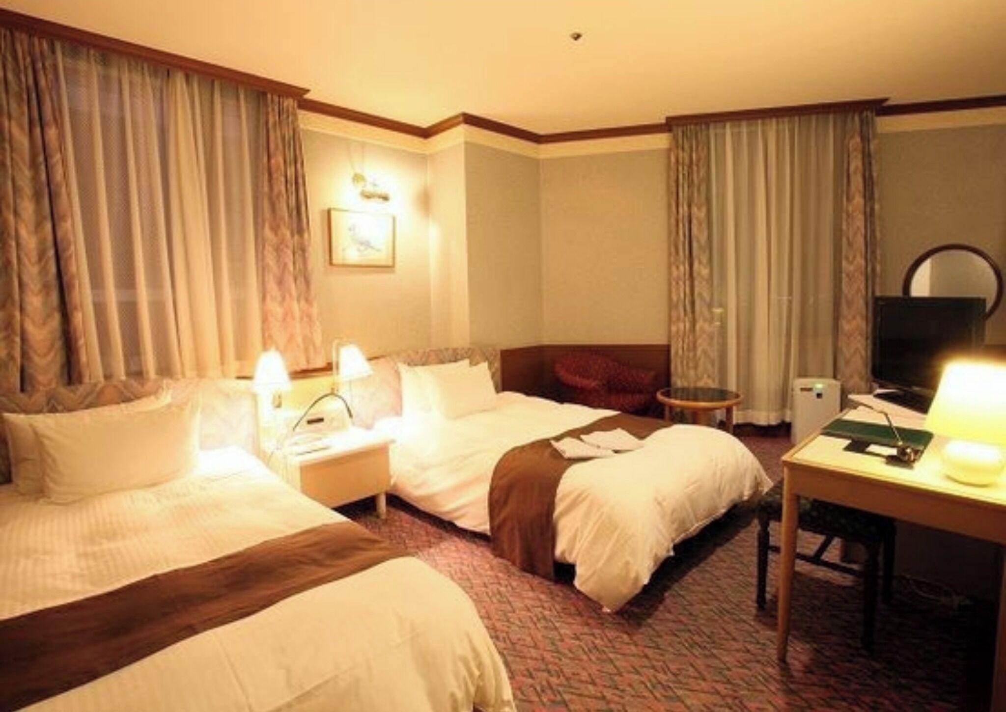 Ein Hotelzimmer mit zwei Betten, einem Schreibtisch, einem Sessel, einem Fernseher und einer Lampe.