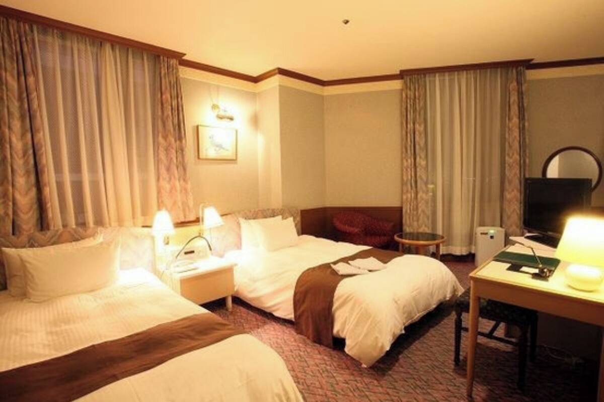 Ein Hotelzimmer mit zwei Betten, einem Schreibtisch, einem Sessel, einem Fernseher und einer Lampe.