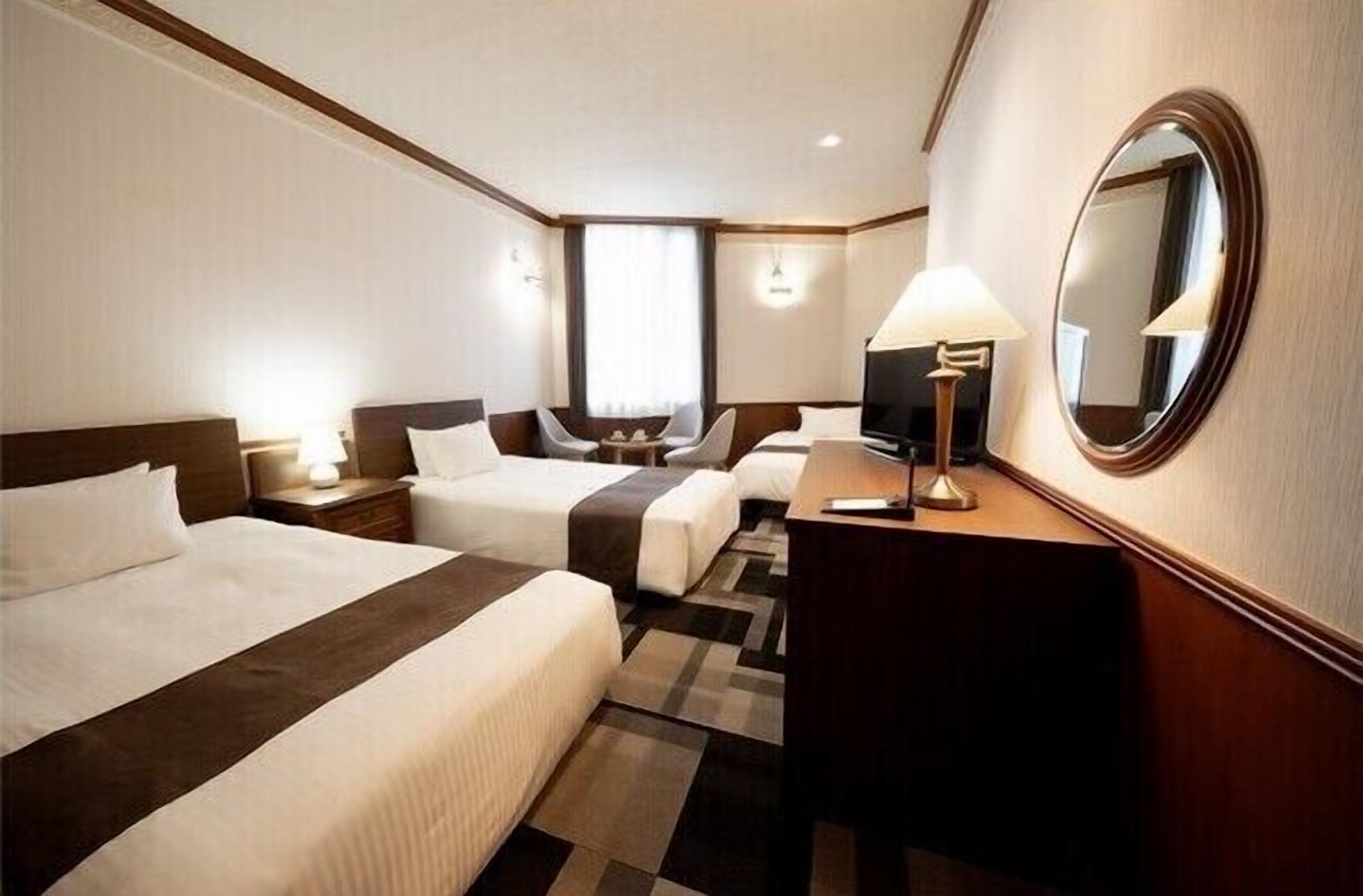 Ein Hotelzimmer mit zwei Betten, einem Schreibtisch, einem Fernseher und einem Spiegel.