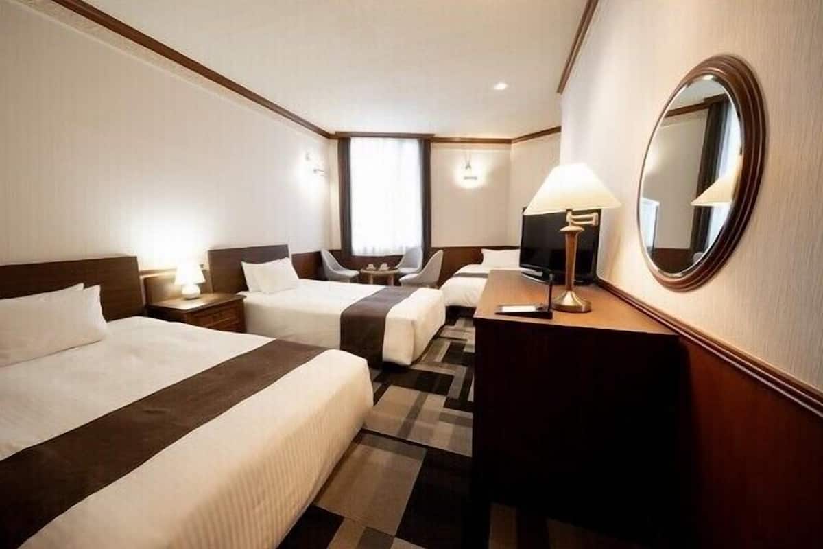 Ein Hotelzimmer mit zwei Betten, einem Schreibtisch, einem Fernseher und einem Spiegel.