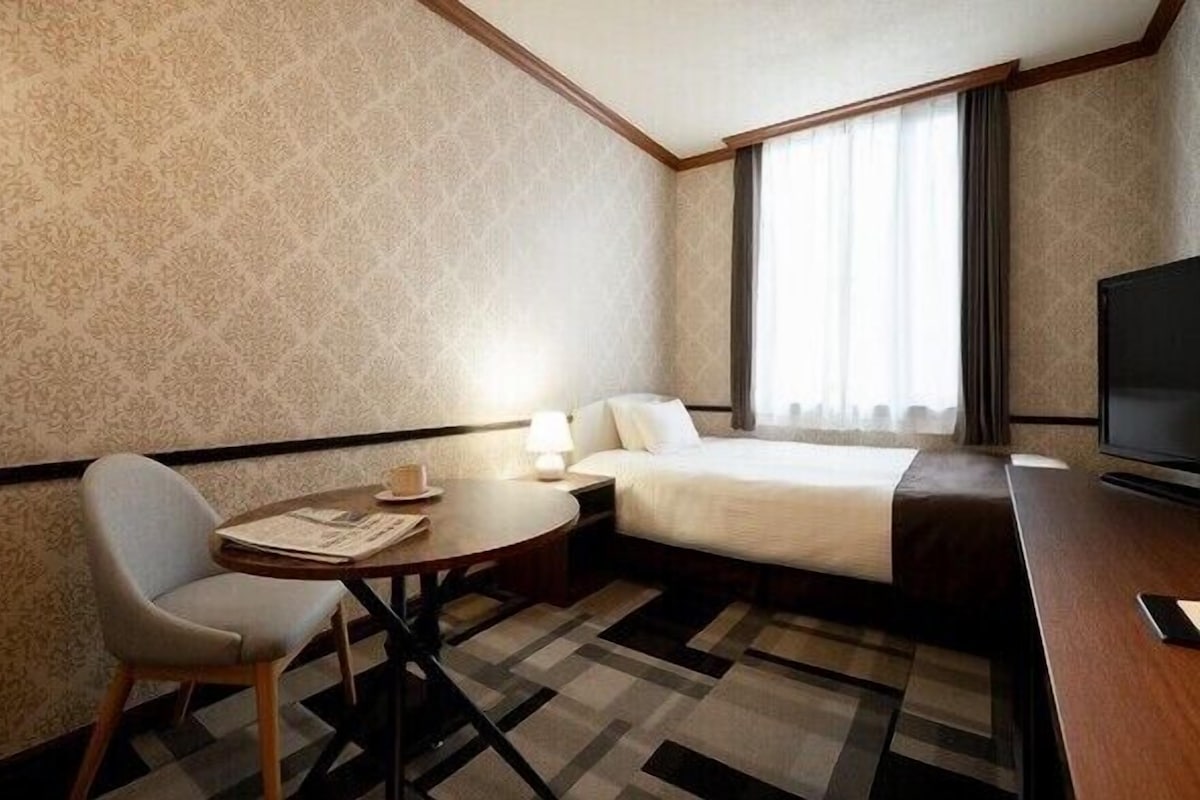 Een hotelkamer met een bed, televisie, bureau, stoel en raam met gordijnen.