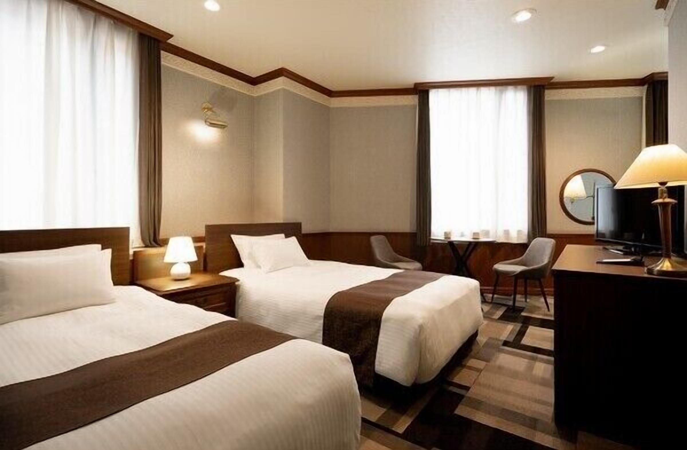 Ein Hotelzimmer mit zwei Betten, einem Schreibtisch, einem Sessel, einem Fernseher und einer Lampe.