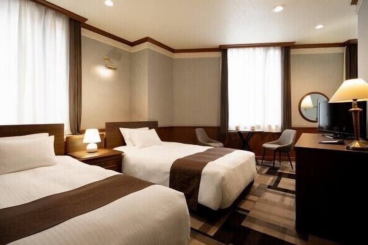 Ein Hotelzimmer mit zwei Betten, einem Schreibtisch, einem Sessel, einem Fernseher und einer Lampe.