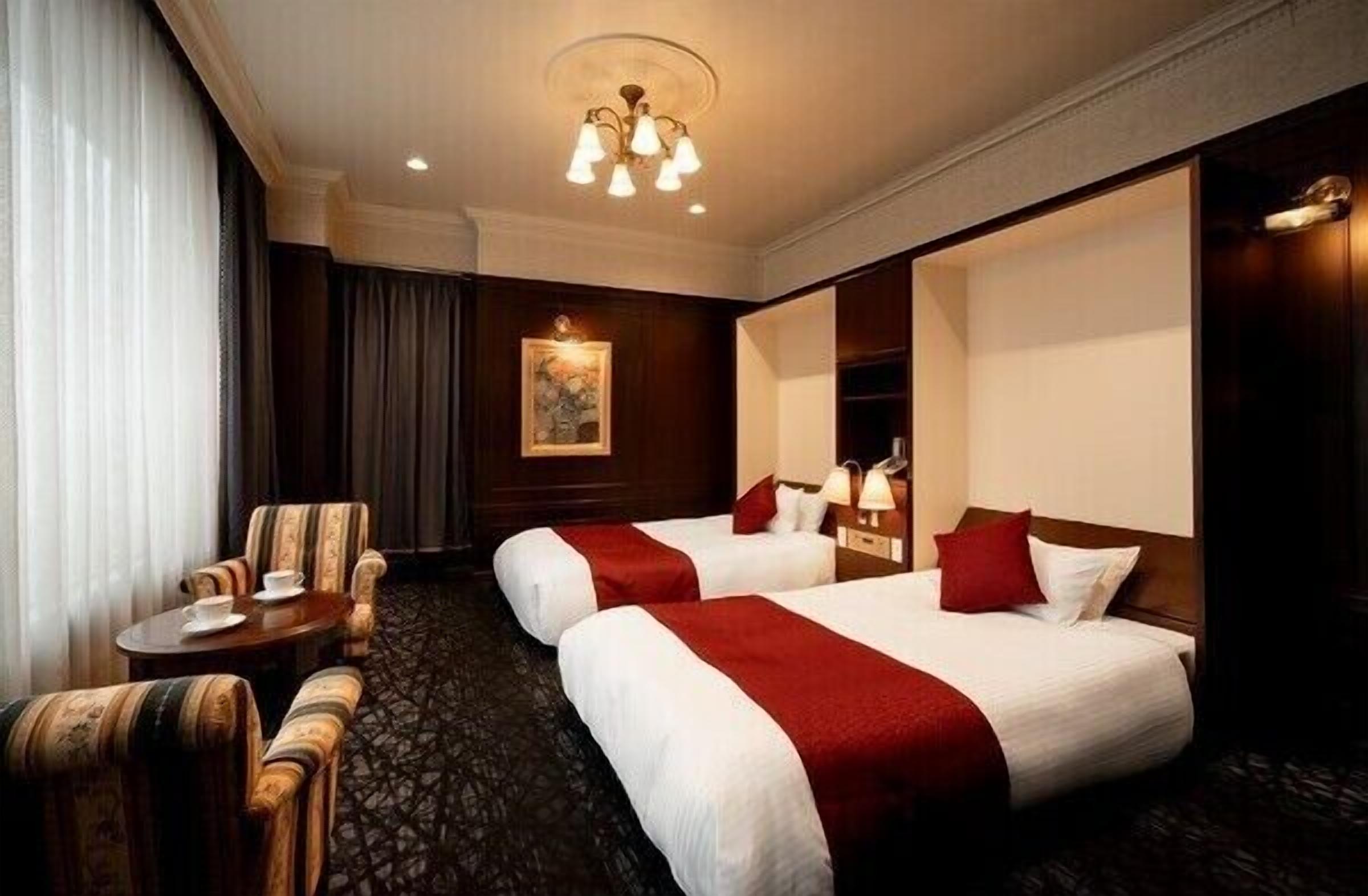 Ein Hotelzimmer mit zwei Betten, einem kleinen Tisch mit Stuhl, einer Chandelier und einem Bild an der Wand.