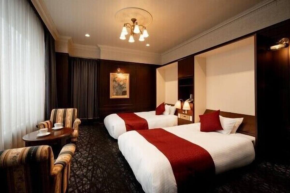 Ein Hotelzimmer mit zwei Betten, einem kleinen Tisch mit Stuhl, einer Chandelier und einem Bild an der Wand.