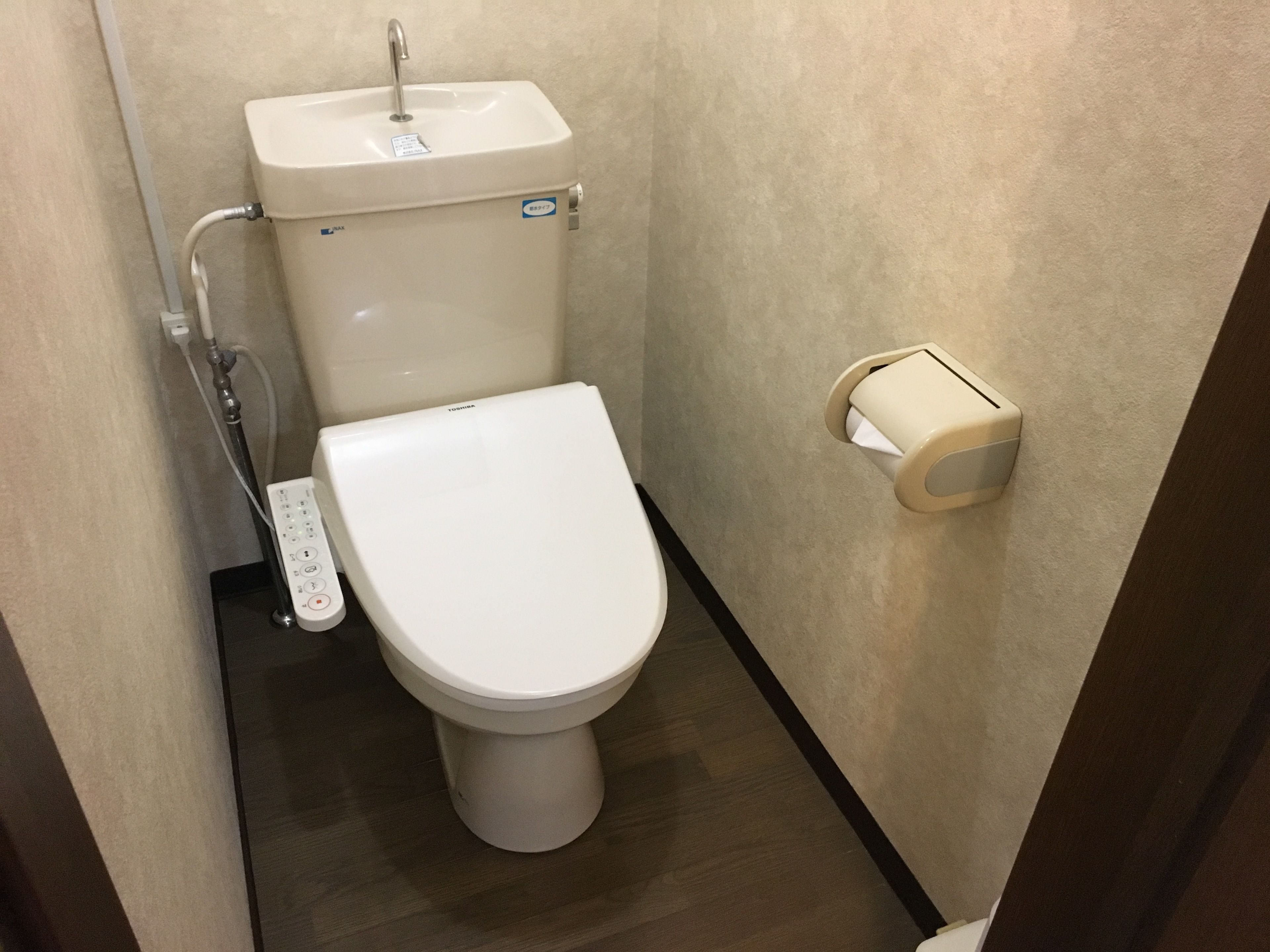 A small, modern bathroom with a white toilet, a wall-mounted sink, and a toilet paper holder.