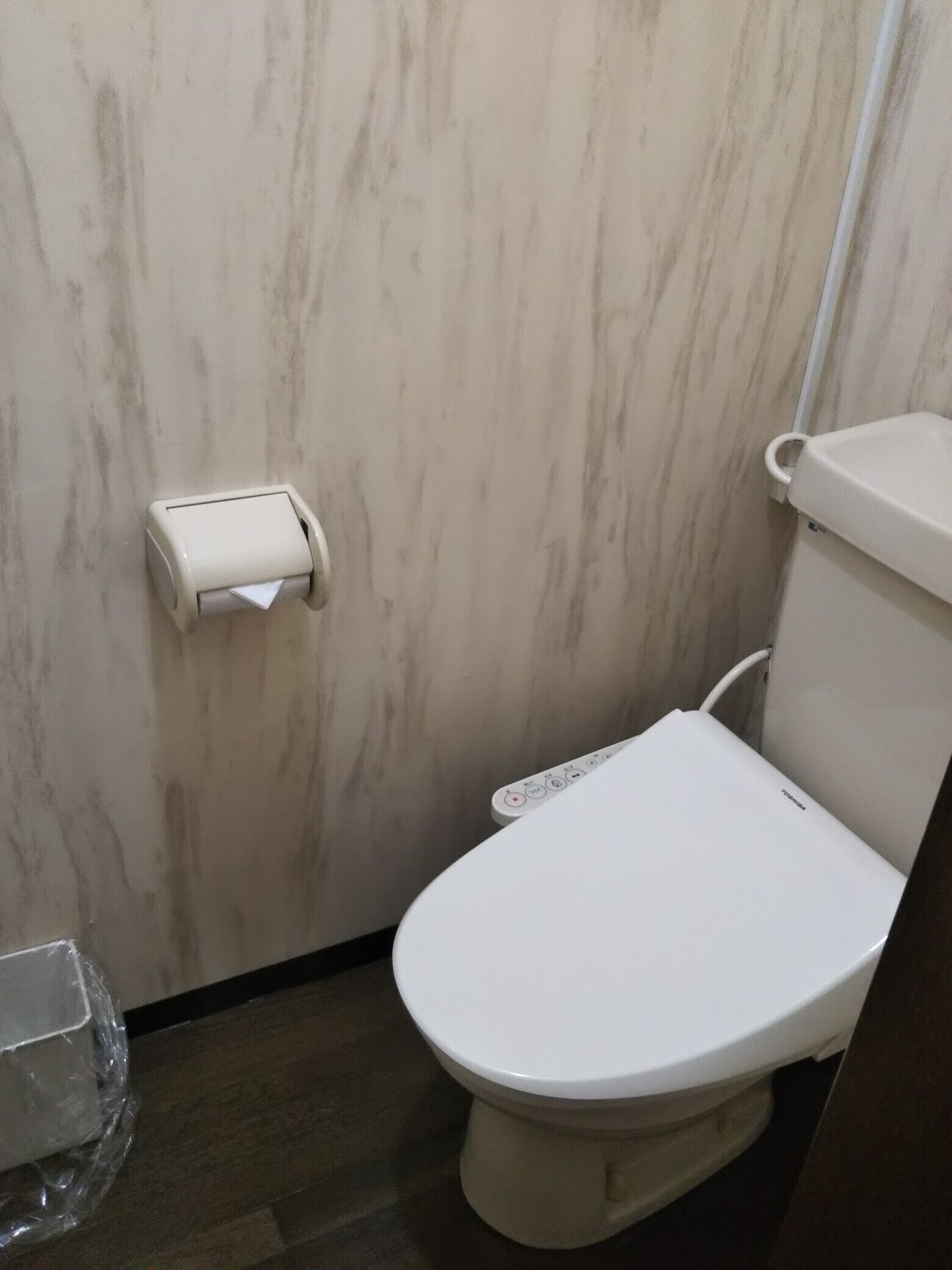 Un inodoro con un panel de control, un dispensador de papel higiénico y un recipiente de plástico en el suelo.