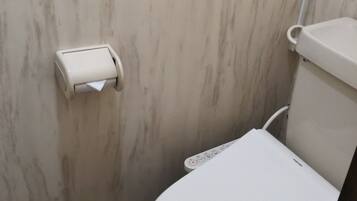 Un inodoro con un panel de control, un dispensador de papel higiénico y un recipiente de plástico en el suelo.