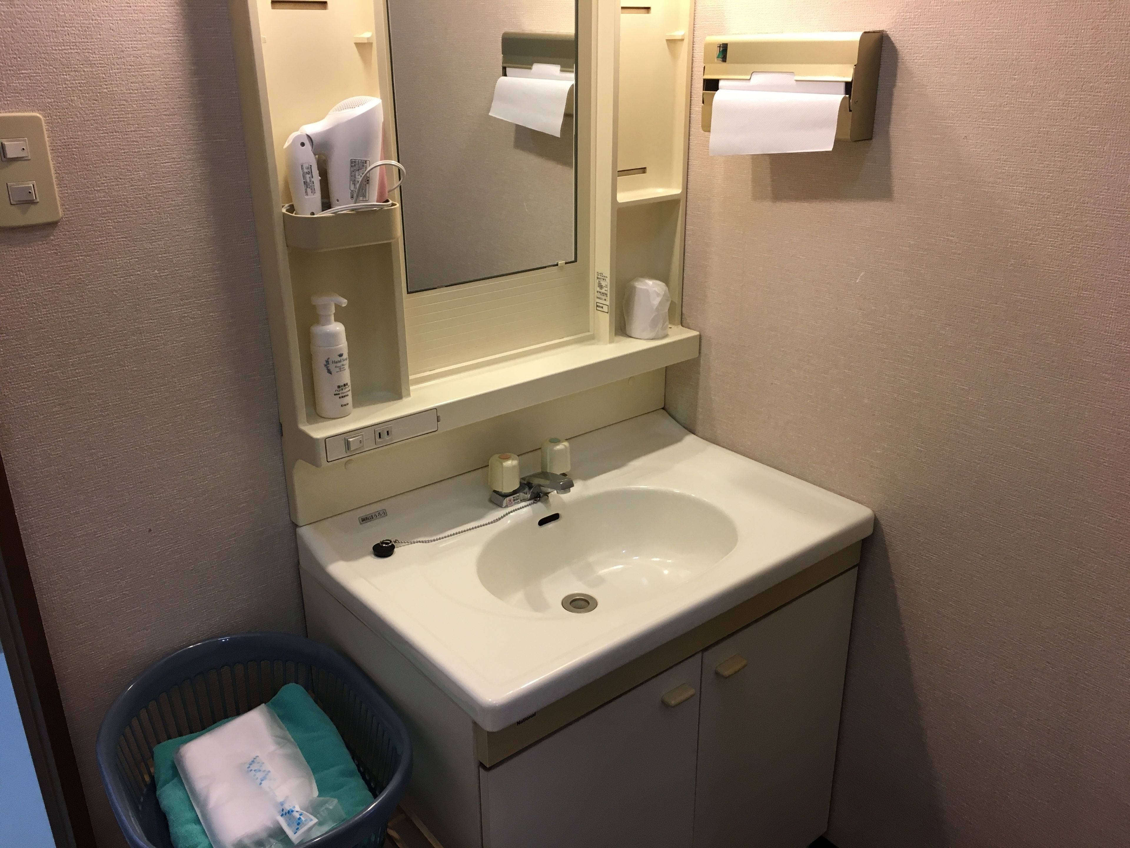 A bathroom with a white sink, a mirror, a towel rack, and a trash bin.