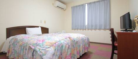 Quarto de hotel com cama, escrivaninha, cadeira, televisão e ar condicionado.