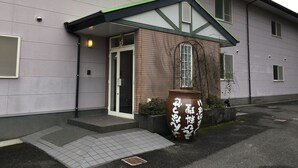 Een hotel ingang met een bord in het Japans, een grote potplant en een betegelde looppad.