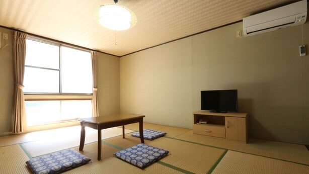 Een kamer met tatami matten, een houten tafel, kussens, een televisie en een airconditioning.