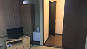 Een kamer met een televisie op een houten kast, een klein plantje, een wit apparaat en een vloer van tatami-matten.
