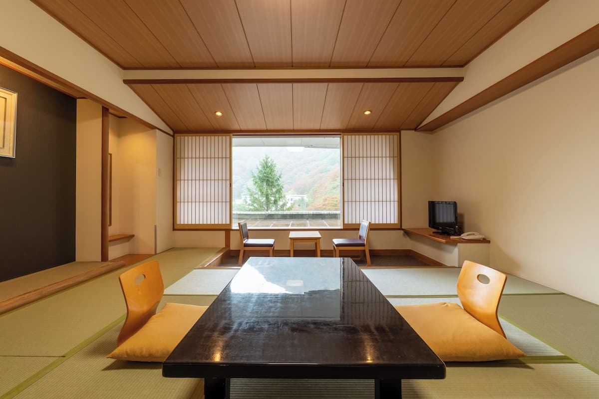 Een traditionele Japanse kamer met tatami vloerbedekking, een lage houten tafel en een televisie op een plank.