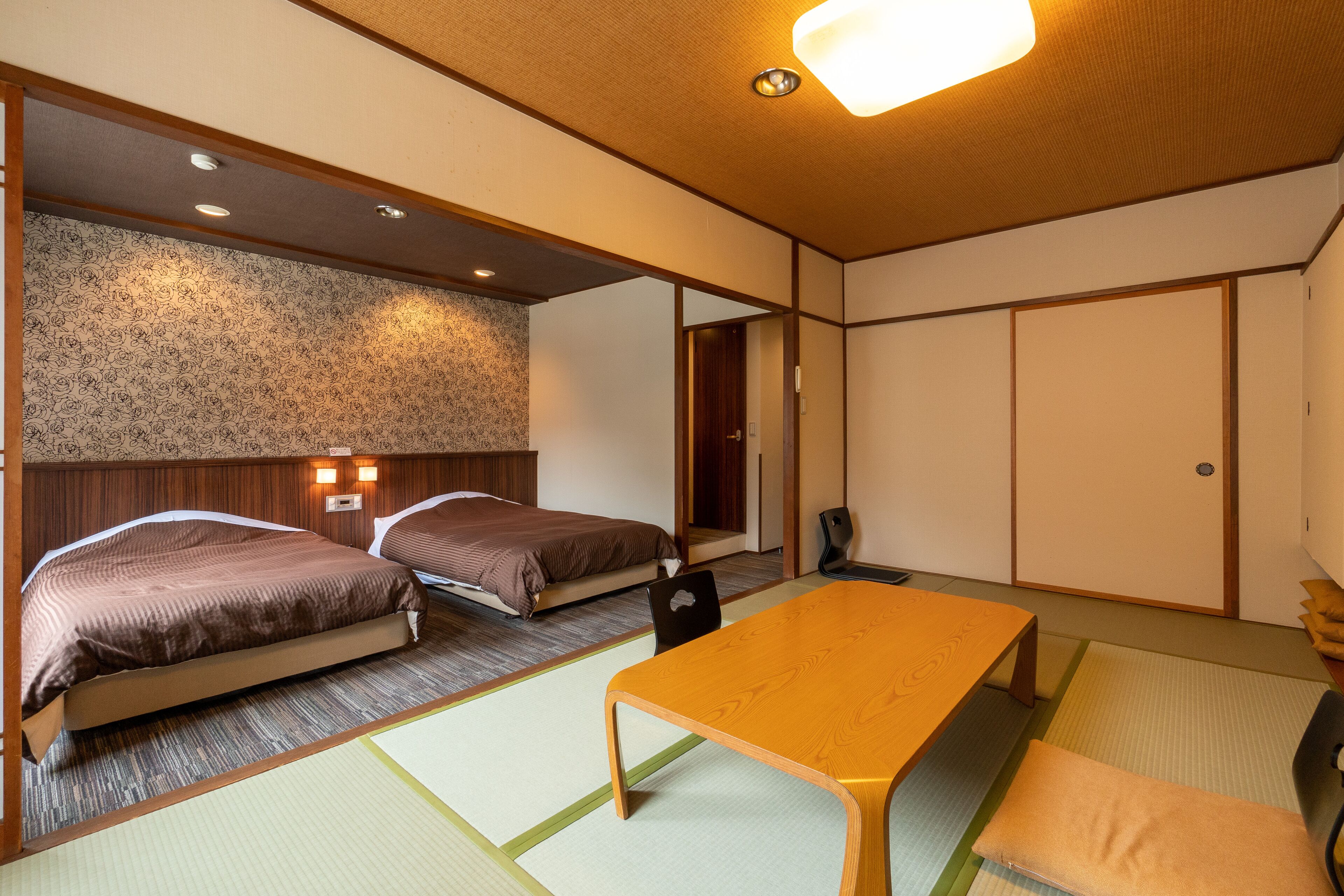 Una habitación de estilo japonés tradicional con suelo de tatami, dos camas, una mesa de madera y una puerta corredera.
