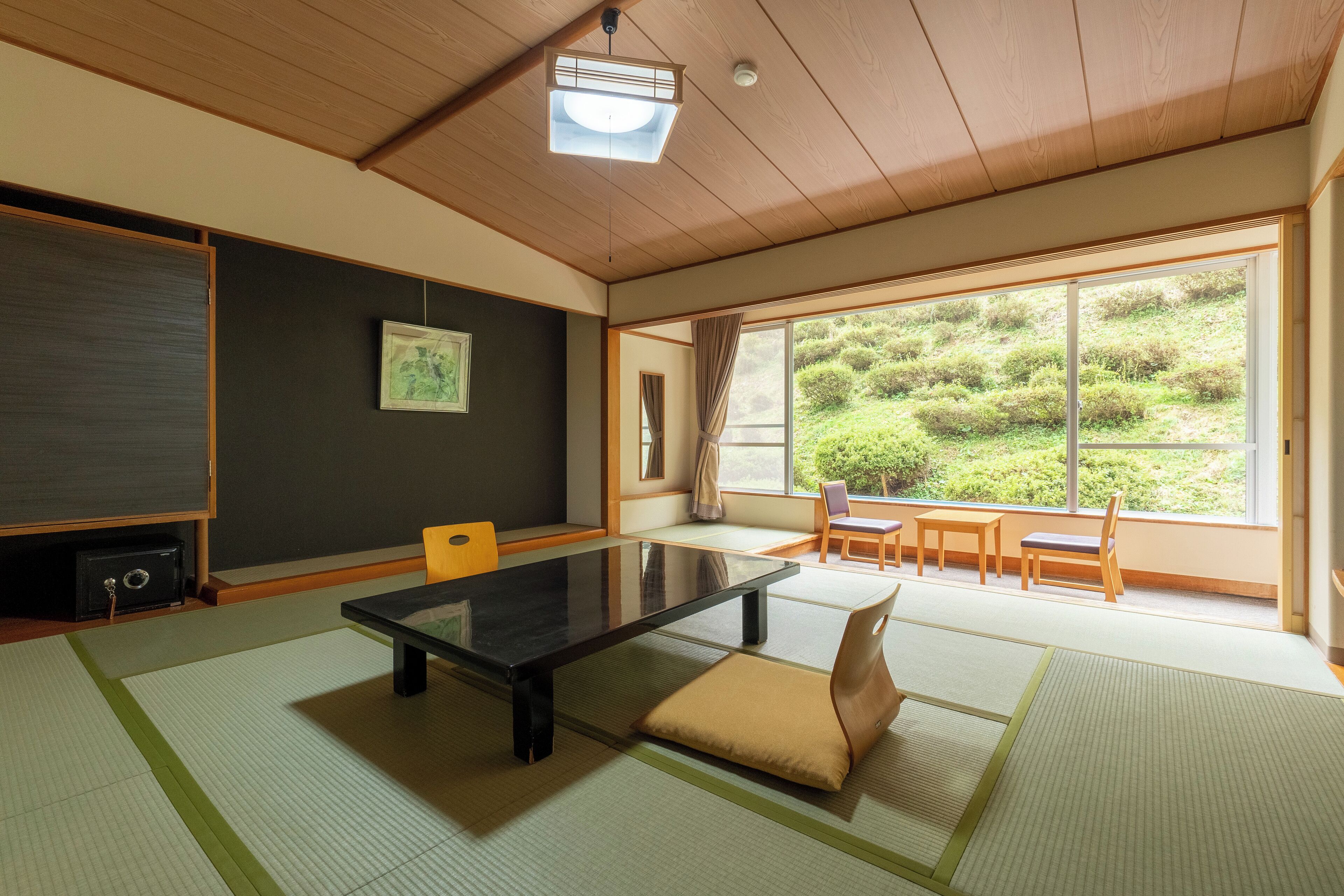 A tatami mat room with a low table, chairs, and a view of greenery outside.