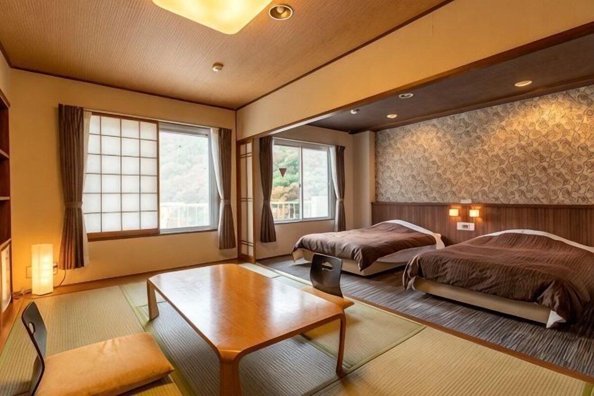 Une pièce de style japonais traditionnel, avec un sol recouvert de tatamis, une table basse, deux lits et une vue sur l’extérieur.