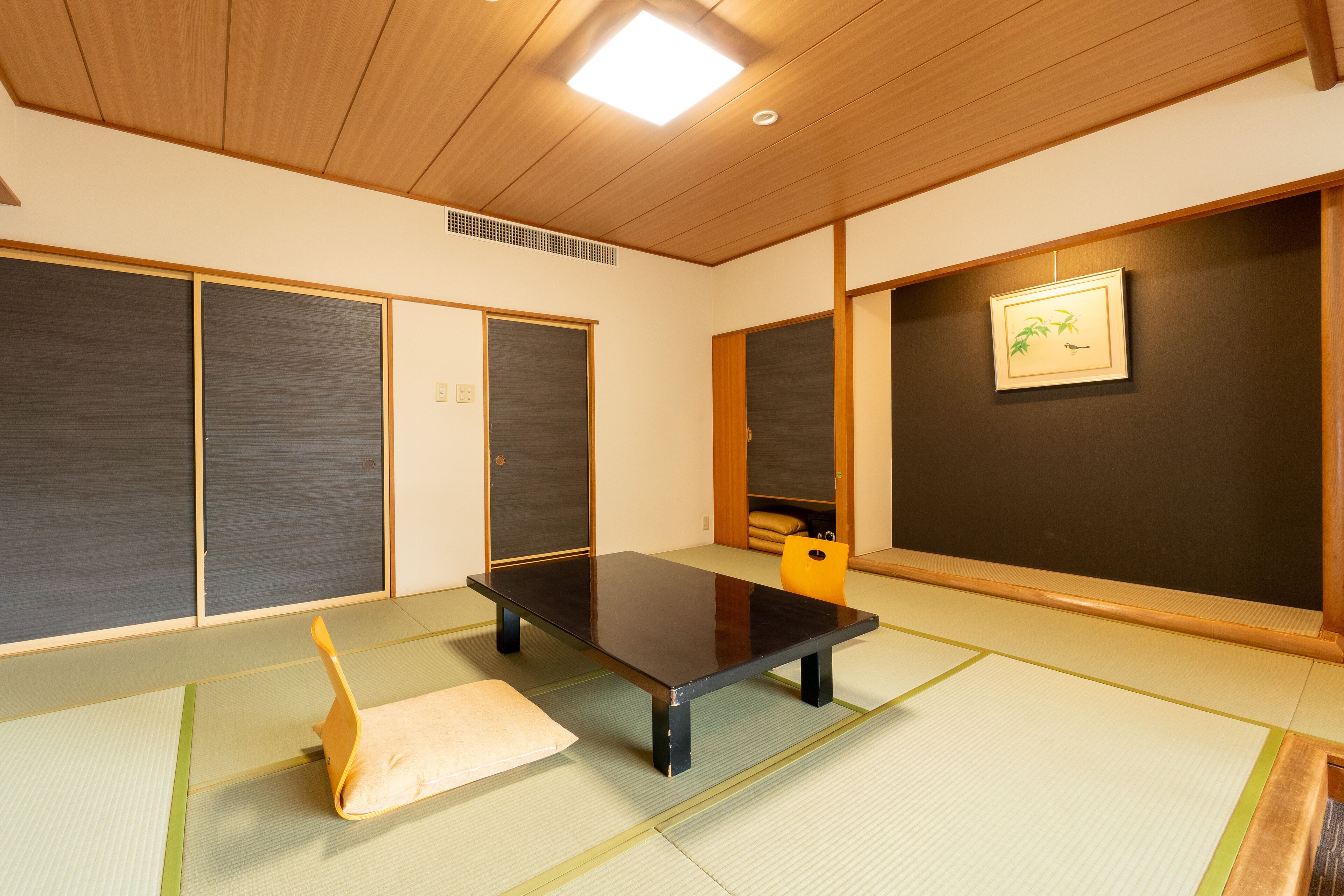 Une pièce avec un sol recouvert de tatamis, une petite table basse, un coussin et des portes coulissantes.