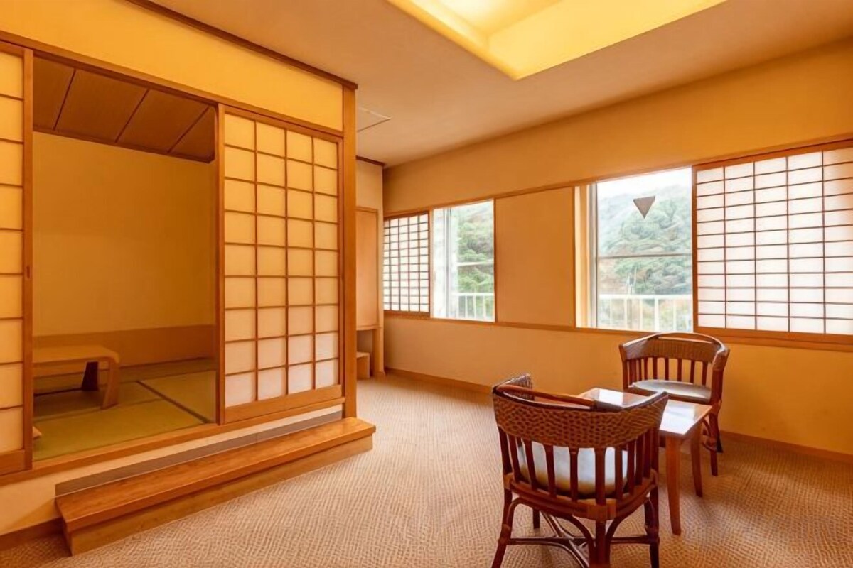 Une pièce de style japonais traditionnel, avec un sol recouvert de tatamis, des portes coulissantes et une petite table basse entourée de chaises.