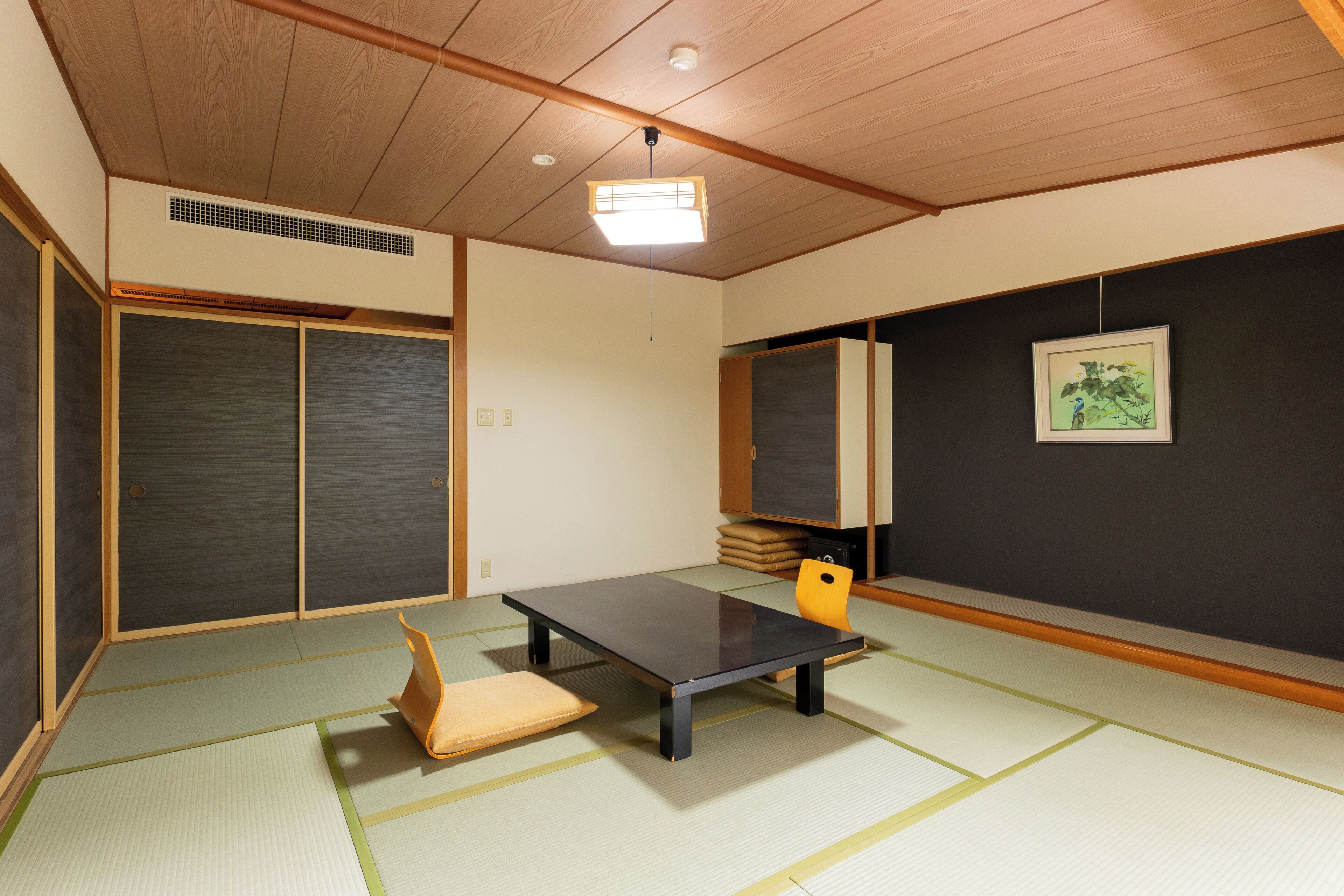 A traditional Japanese room with tatami flooring, a low table, a cushion, sliding doors, and a framed picture on the wall.