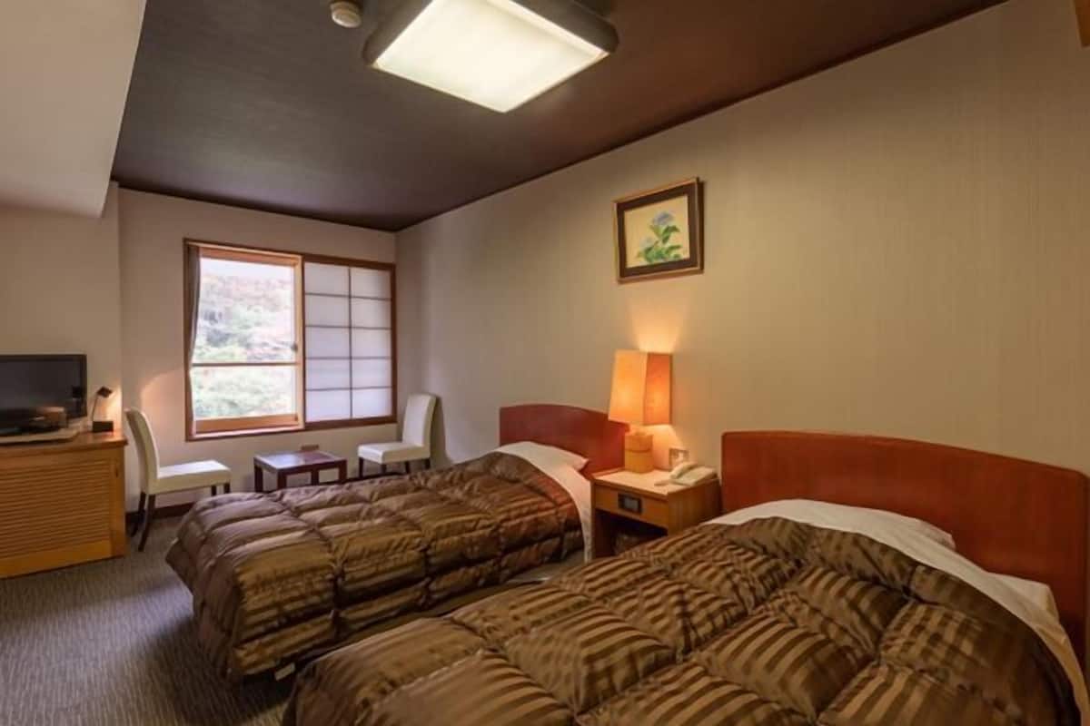 Een hotelkamer met twee bedden, een bureau, een stoel, een raam en een schilderij aan de muur.