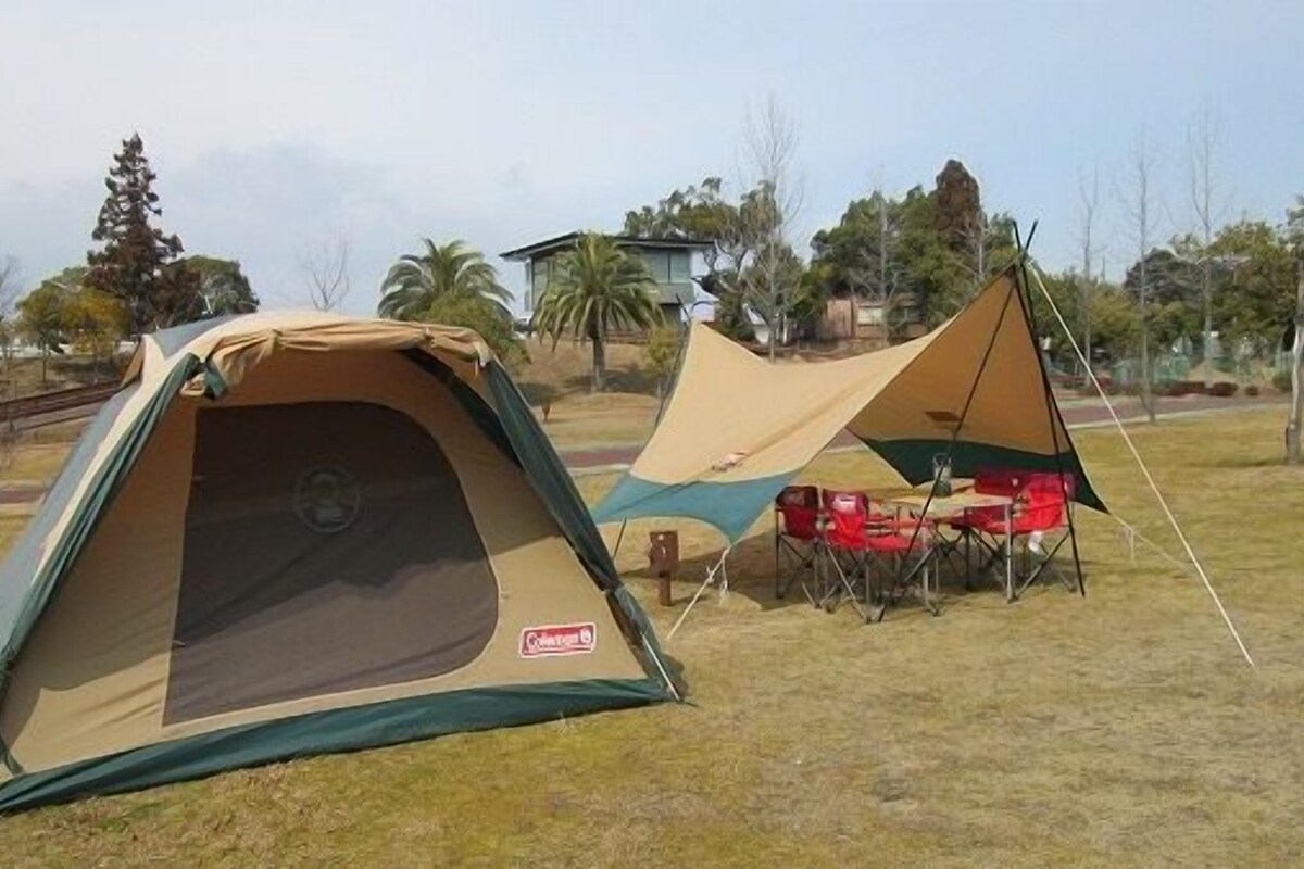 Two tents in a grassy field with trees and a building in the background.