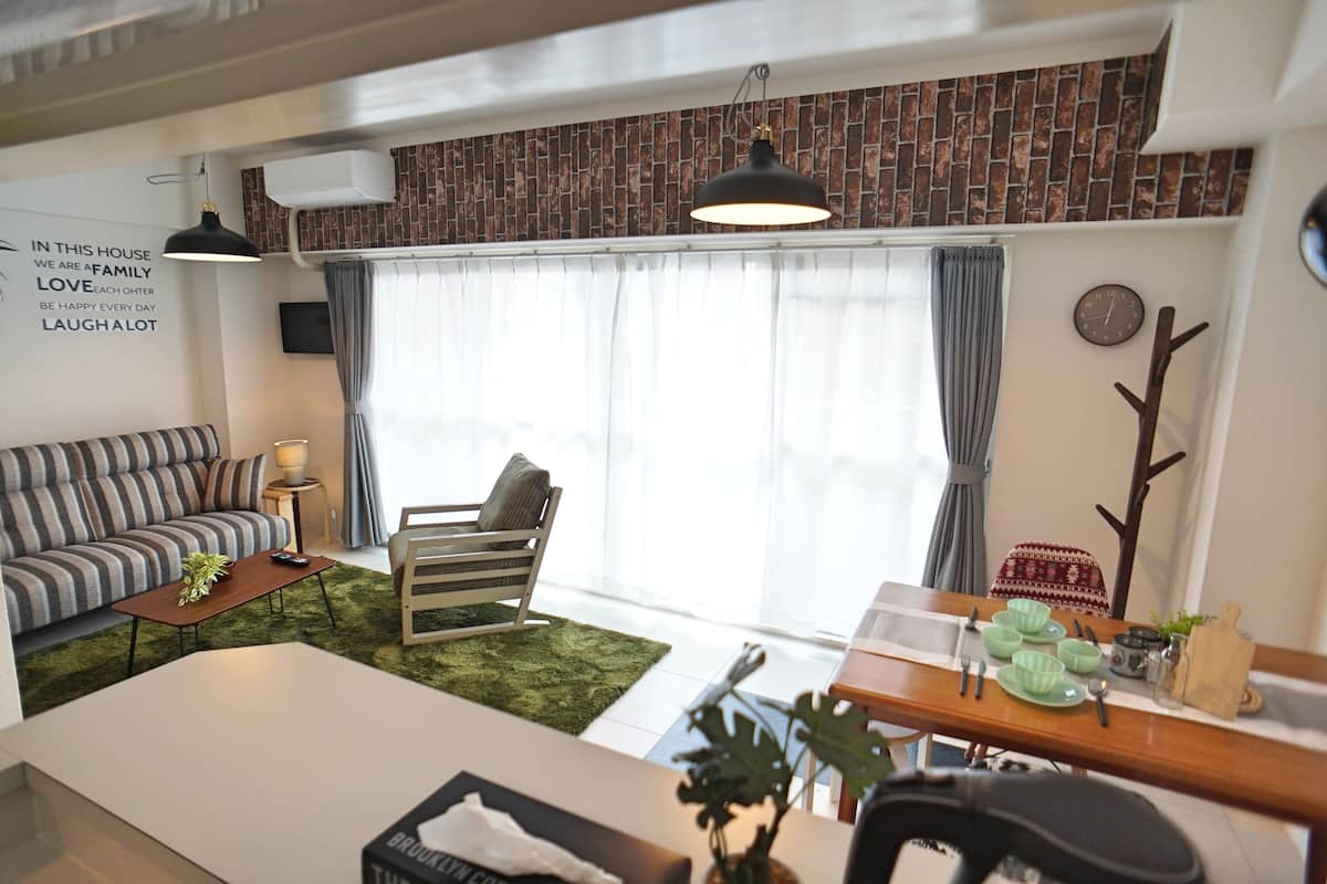 Una sala de estar moderna con un sofá, una silla, una mesa de comedor con cuencos y utensilios, y una planta decorativa.