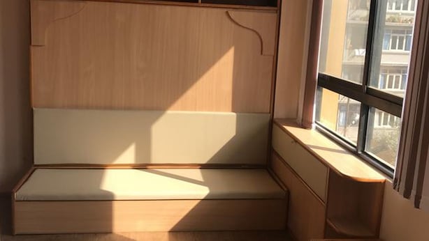 Un coin de pièce avec un banc en bois, une petite table et une fenêtre donnant sur des immeubles.