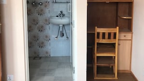 Une salle de bain avec un lavabo, des toilettes et une douche. On y trouve une chaise en bois et un petit meuble en bois.