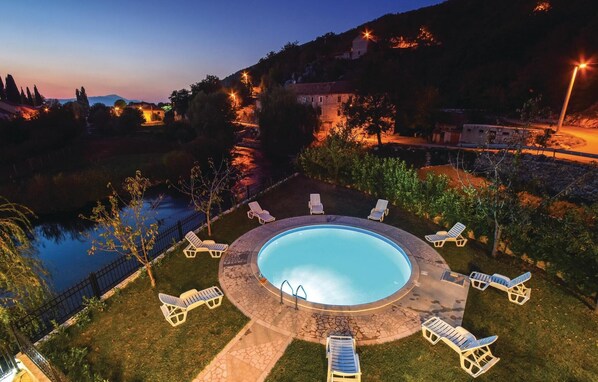 A circular pool with lounge chairs around it, surrounded by a stone patio and a view of a body of water and hills. - Gorgeous home in Grab (Grab)