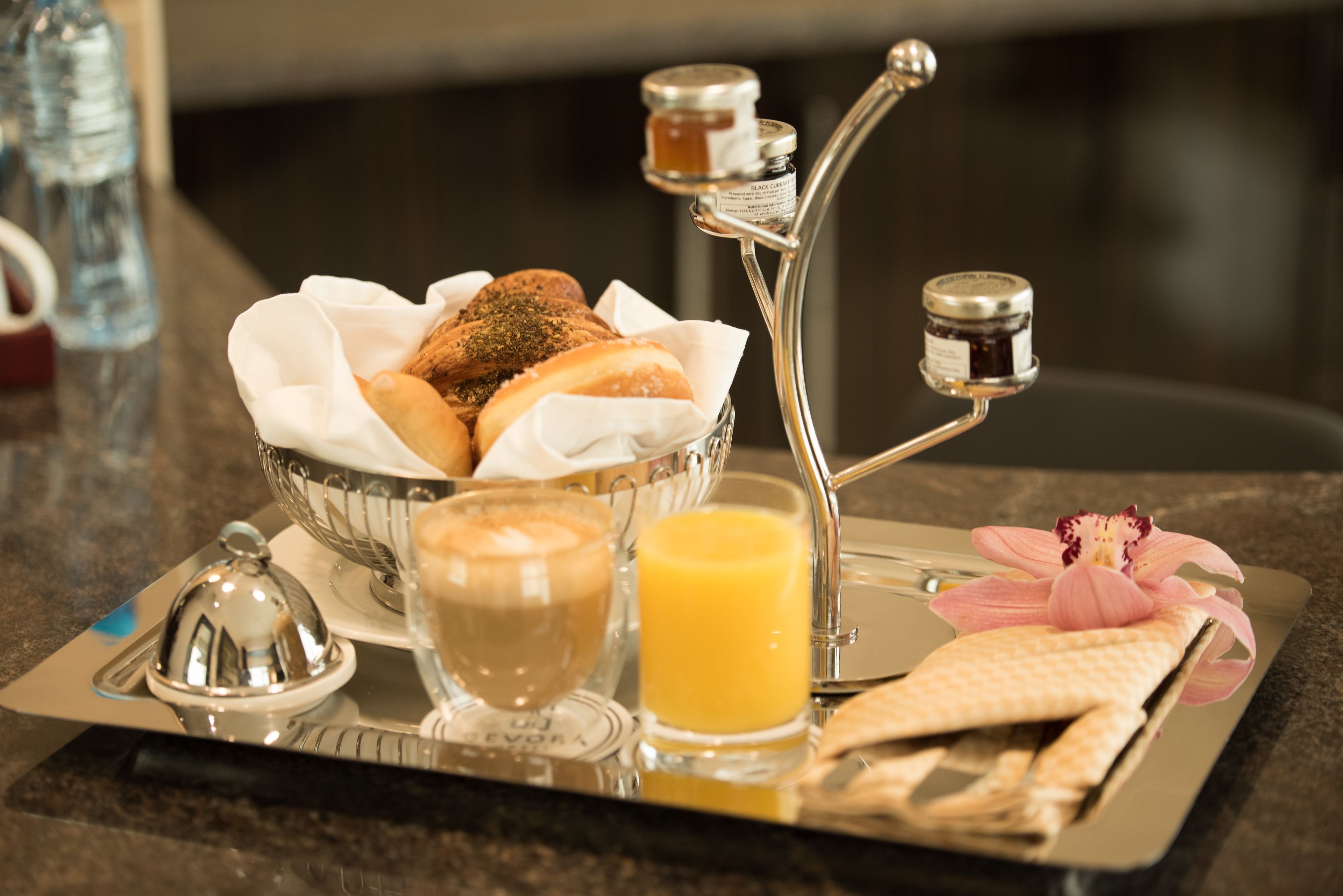 A breakfast tray with bread, a coffee cup, a glass of orange juice, and condiments on a tray.