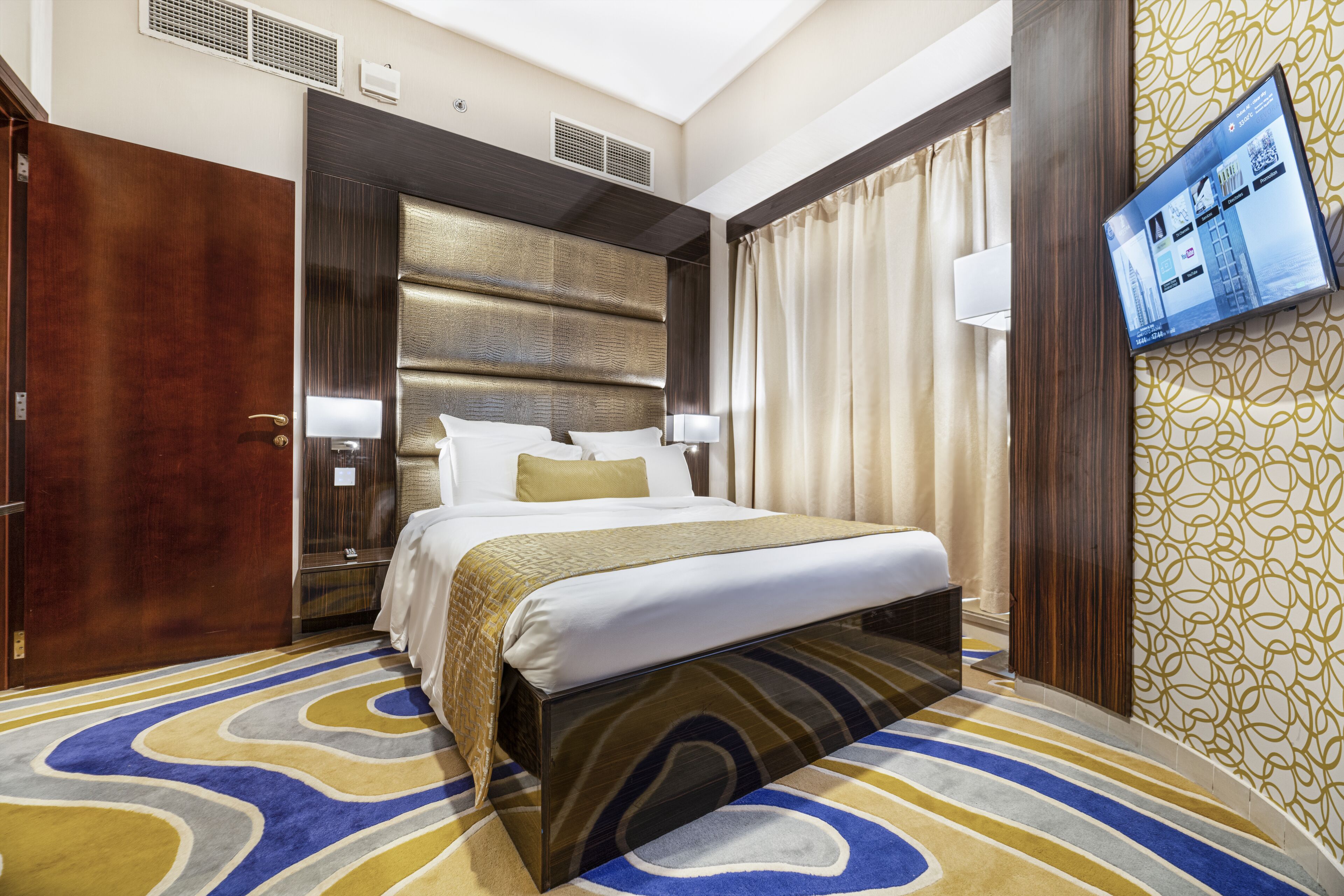 Une chambre d’hôtel avec un grand lit, un téléviseur à écran plat fixé au mur et une moquette à motifs.