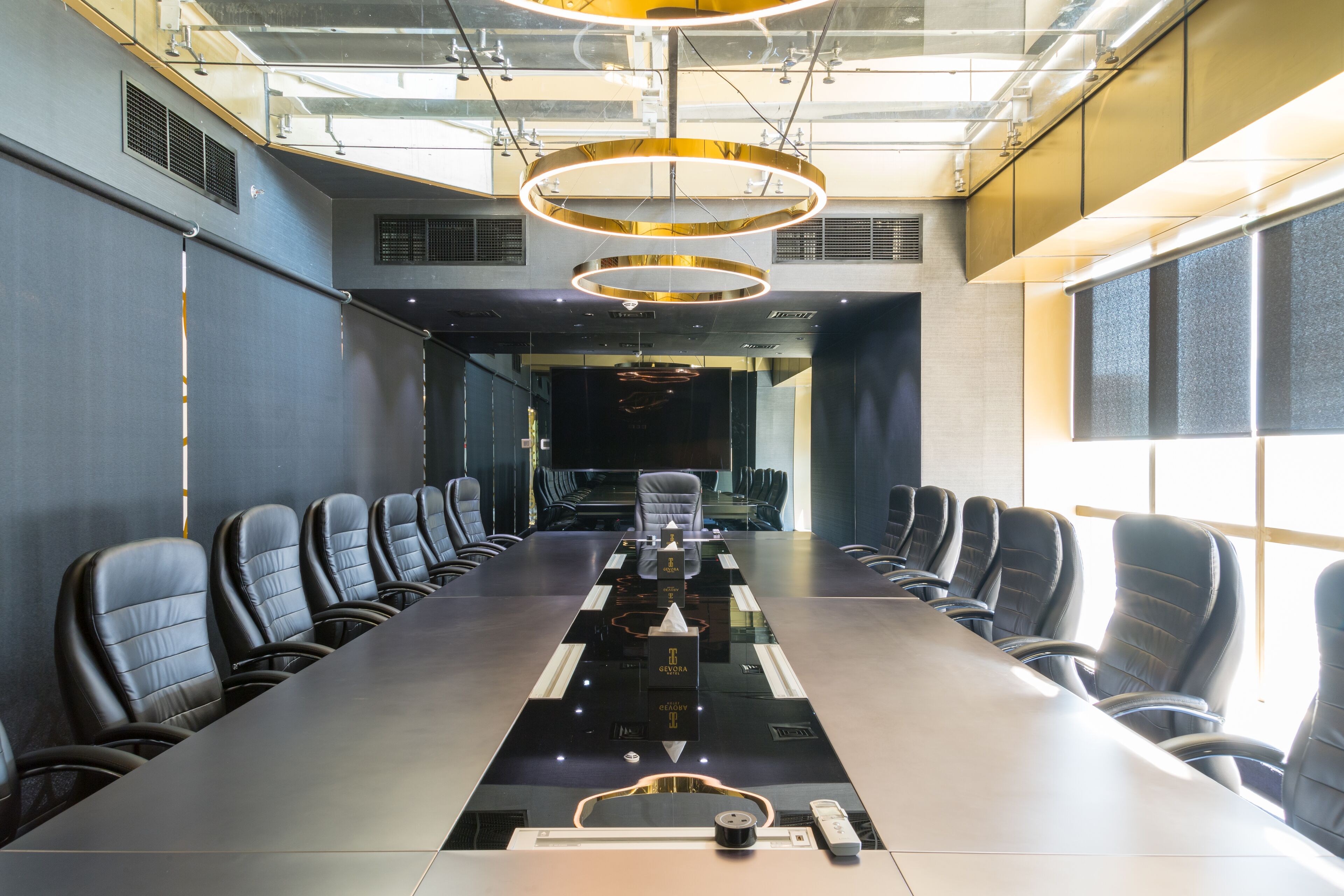 A conference room with a long table, black leather chairs, and a modern chandelier.