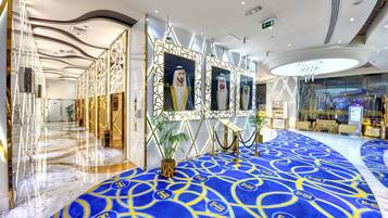 A spacious lobby with a blue carpet, gold accents, and a modern chandelier.