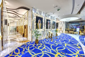 A spacious lobby with a blue carpet, gold accents, and a modern chandelier.