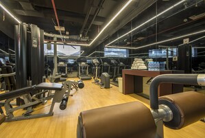 Un gimnasio con varias máquinas de ejercicio, suelo de madera y un espejo grande.