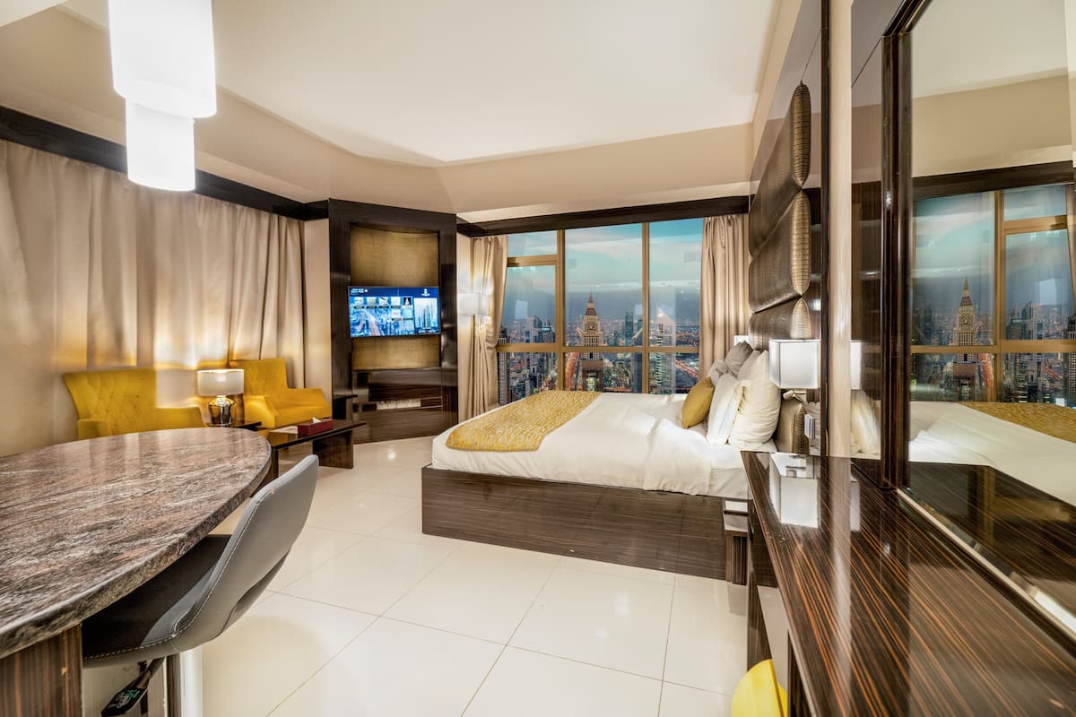Une chambre d’hôtel moderne dotée d’un grand lit, d’un coin repas et d’un téléviseur diffusant des images de la ville.