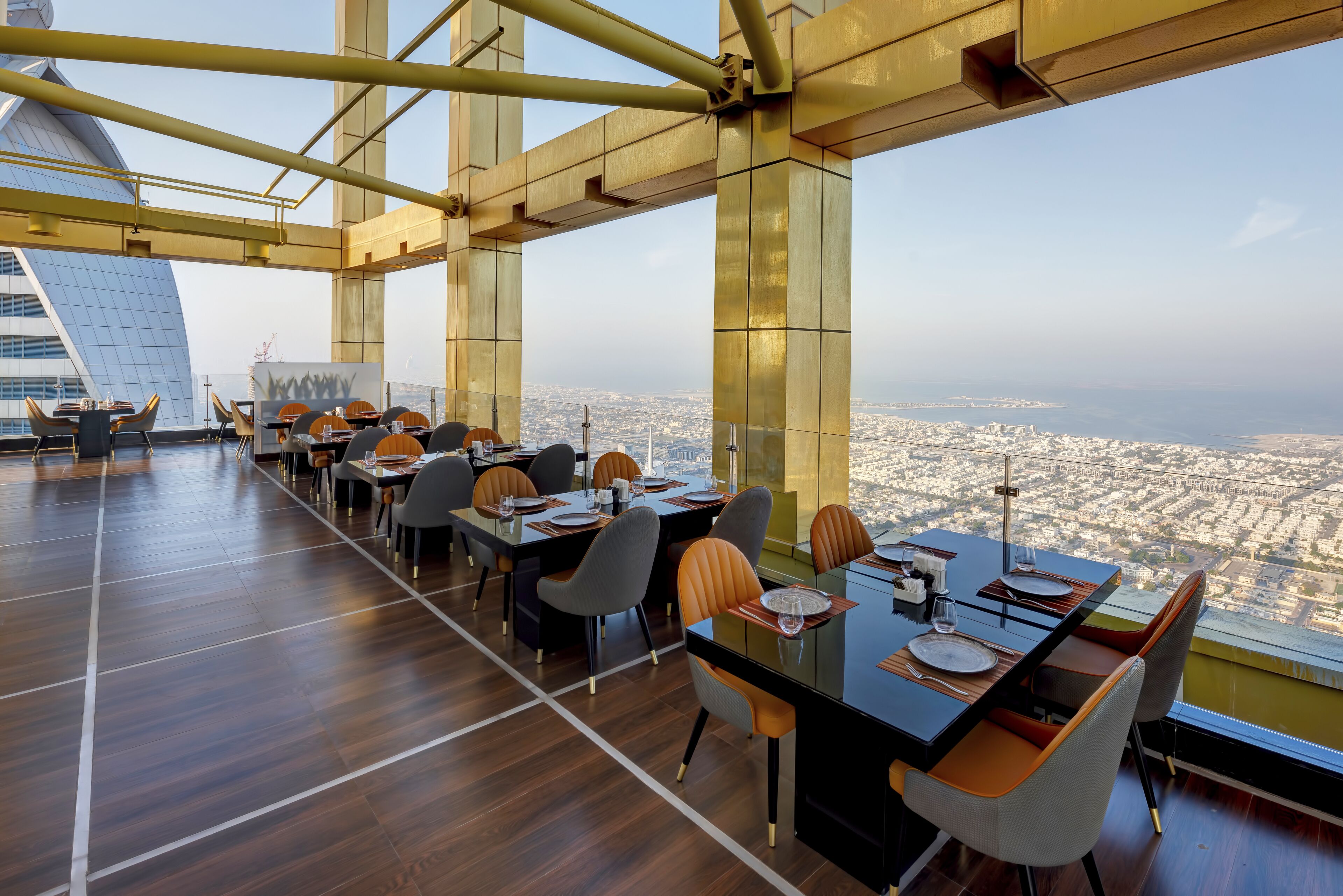 A modern dining area with a city view, featuring a long table with chairs, a glass partition, and a high ceiling with structural beams.