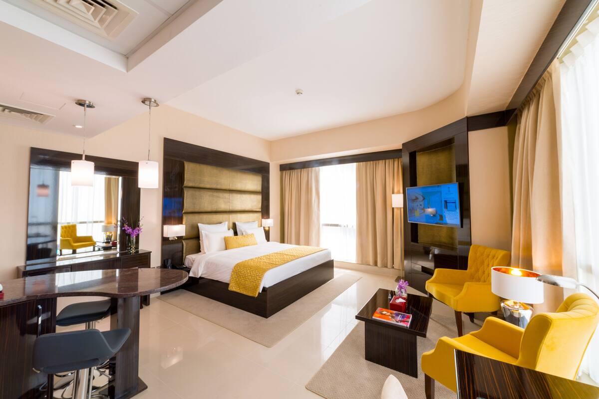 Une chambre d’hôtel moderne dotée d’un grand lit, d’un bureau avec une chaise, d’un canapé, d’une télévision et d’une grande fenêtre avec des rideaux.