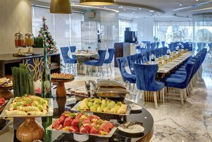 A buffet with various food items, a Christmas tree, and a long dining table with blue chairs.
