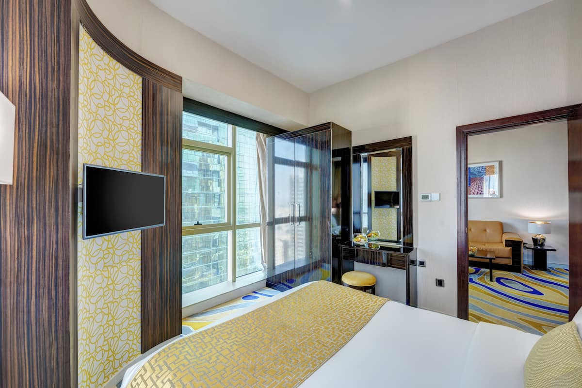 Une chambre d’hôtel avec un grand lit, une télévision, une salle de bain avec un miroir et une fenêtre avec des rideaux.