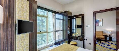 Habitación de hotel con una cama grande, televisión, baño con espejo y ventana con cortinas.