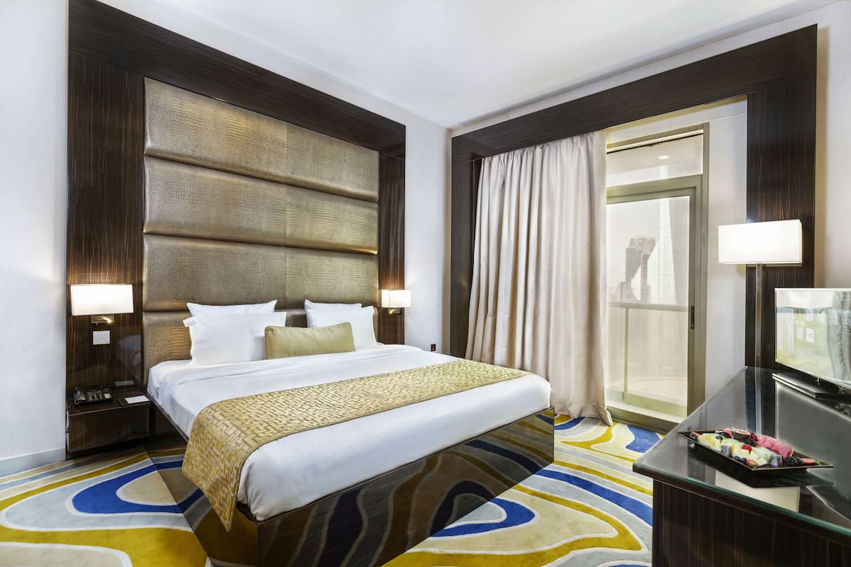 Une chambre d’hôtel avec un grand lit, un bureau doté d’un téléviseur à écran plat, une table de chevet avec une lampe et une fenêtre avec des rideaux.