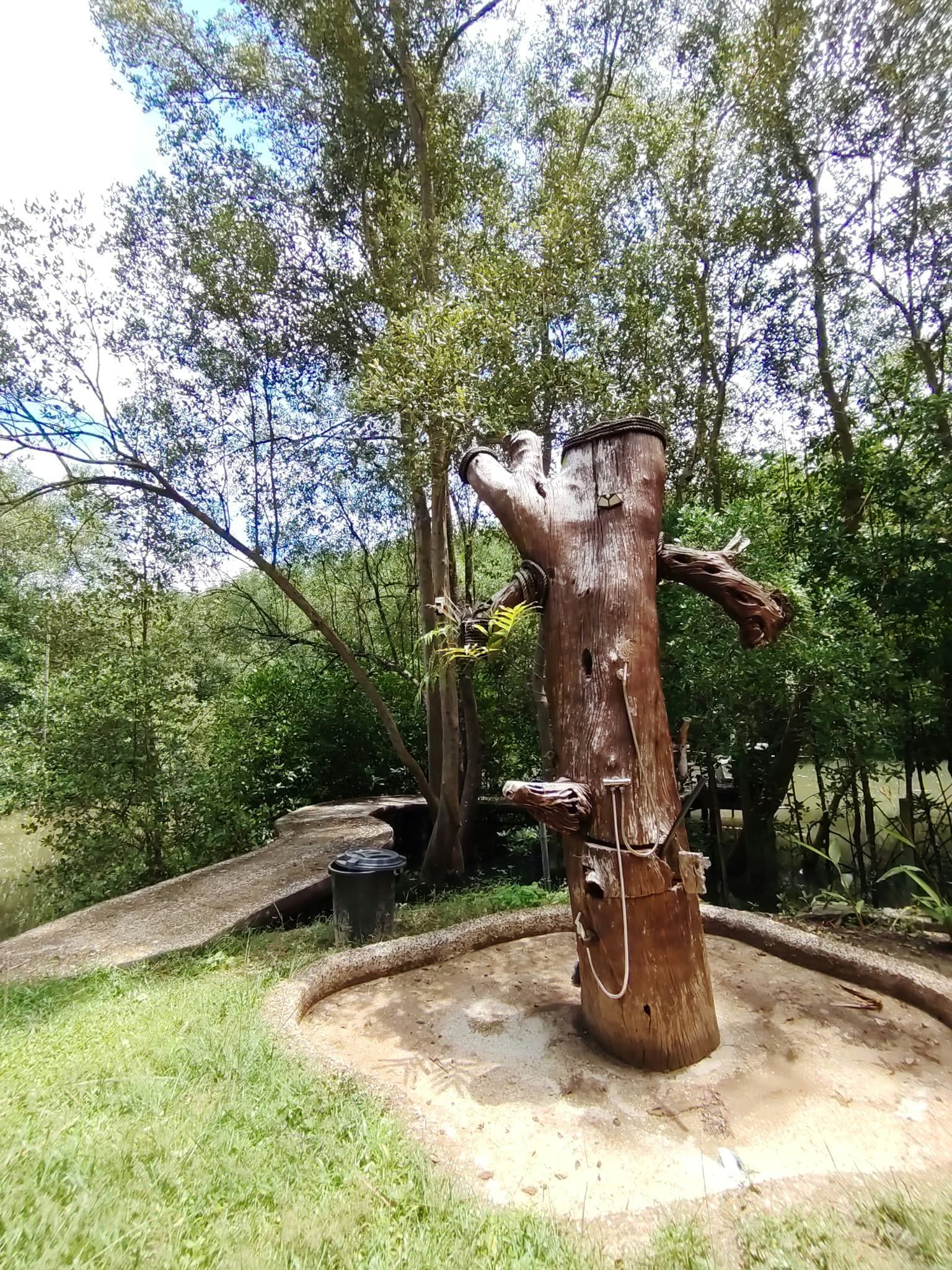 A large wooden sculpture in a natural setting with a circular stone platform.