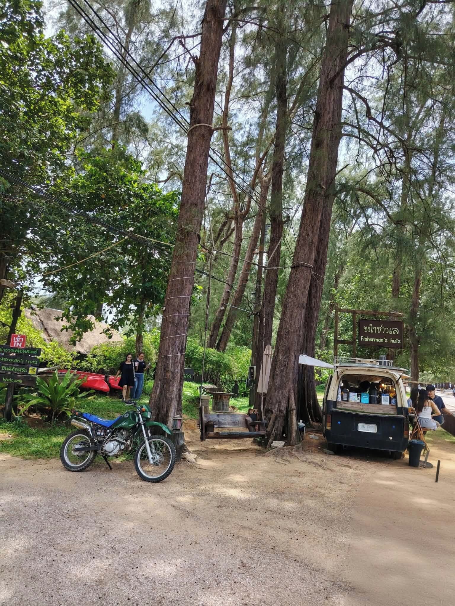 Zona boscosa con un cartel de Fisherman's Huts, una motocicleta y un vehículo con cubierta.