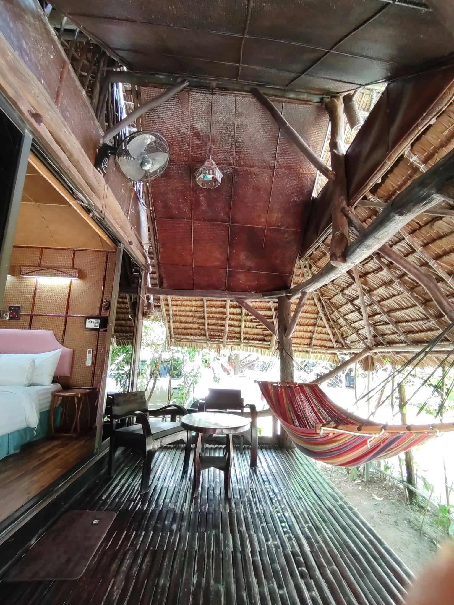 A room with a wooden ceiling, a fan, a hammock, and a bed with a pillow.