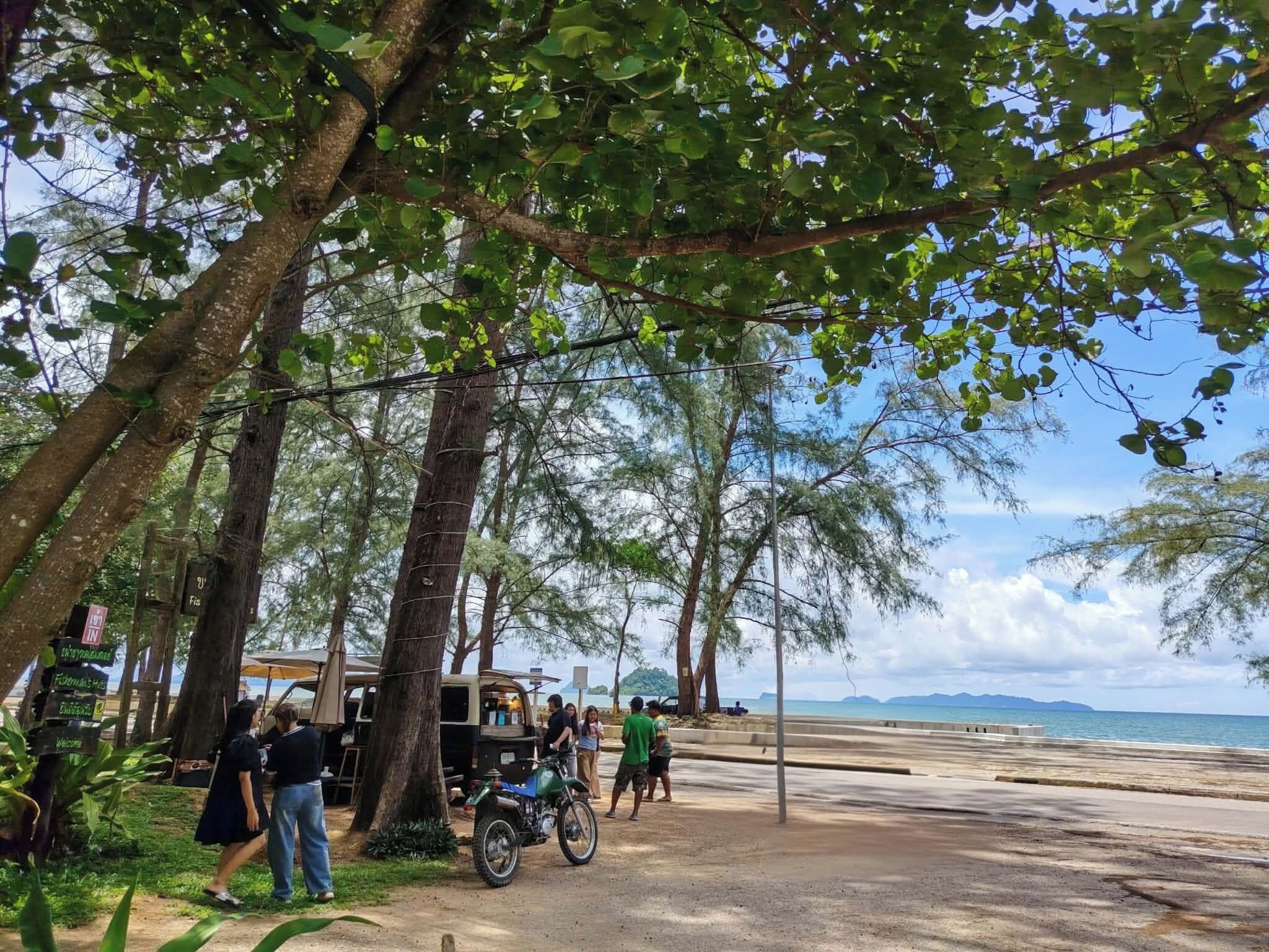 A beachside area with trees, a parked motorcycle, and a vehicle with a signboard.