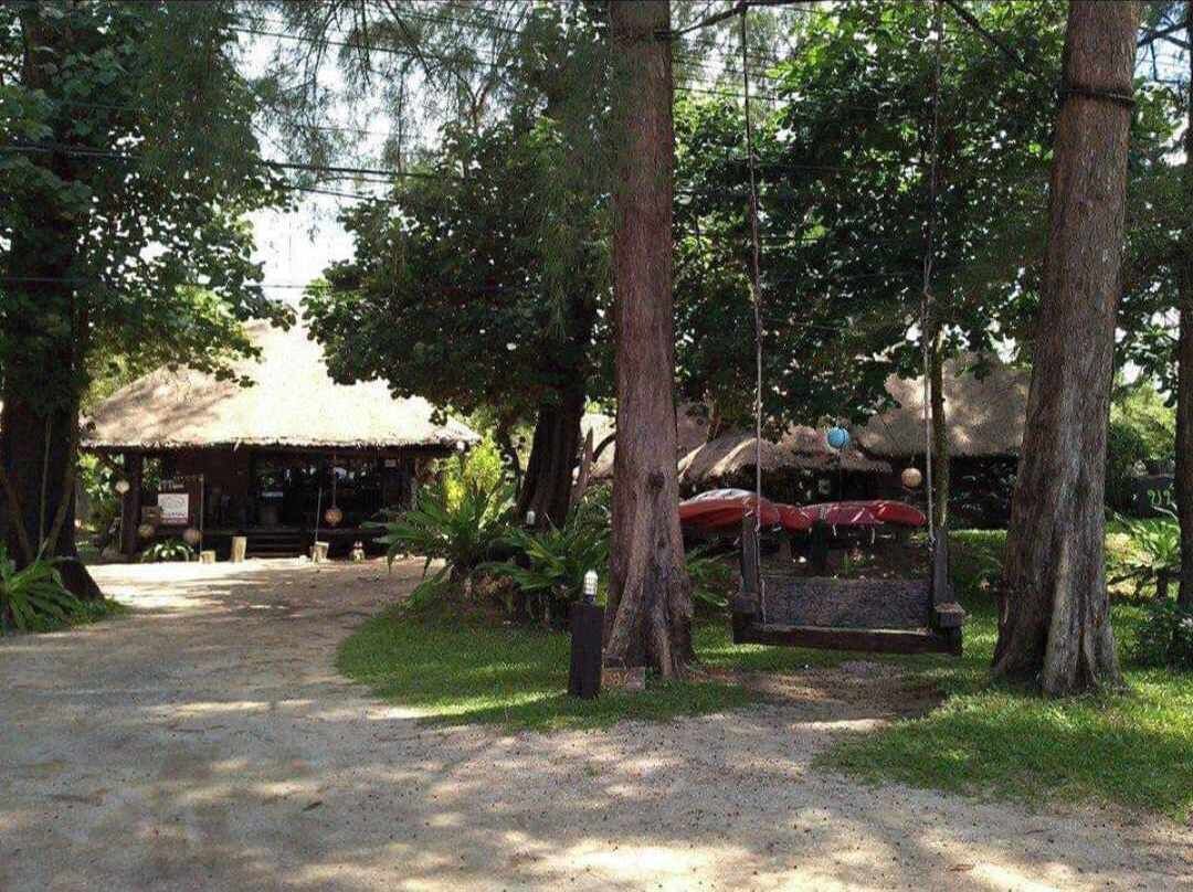 A rustic wooden building with a thatched roof, surrounded by trees and a gravel path.